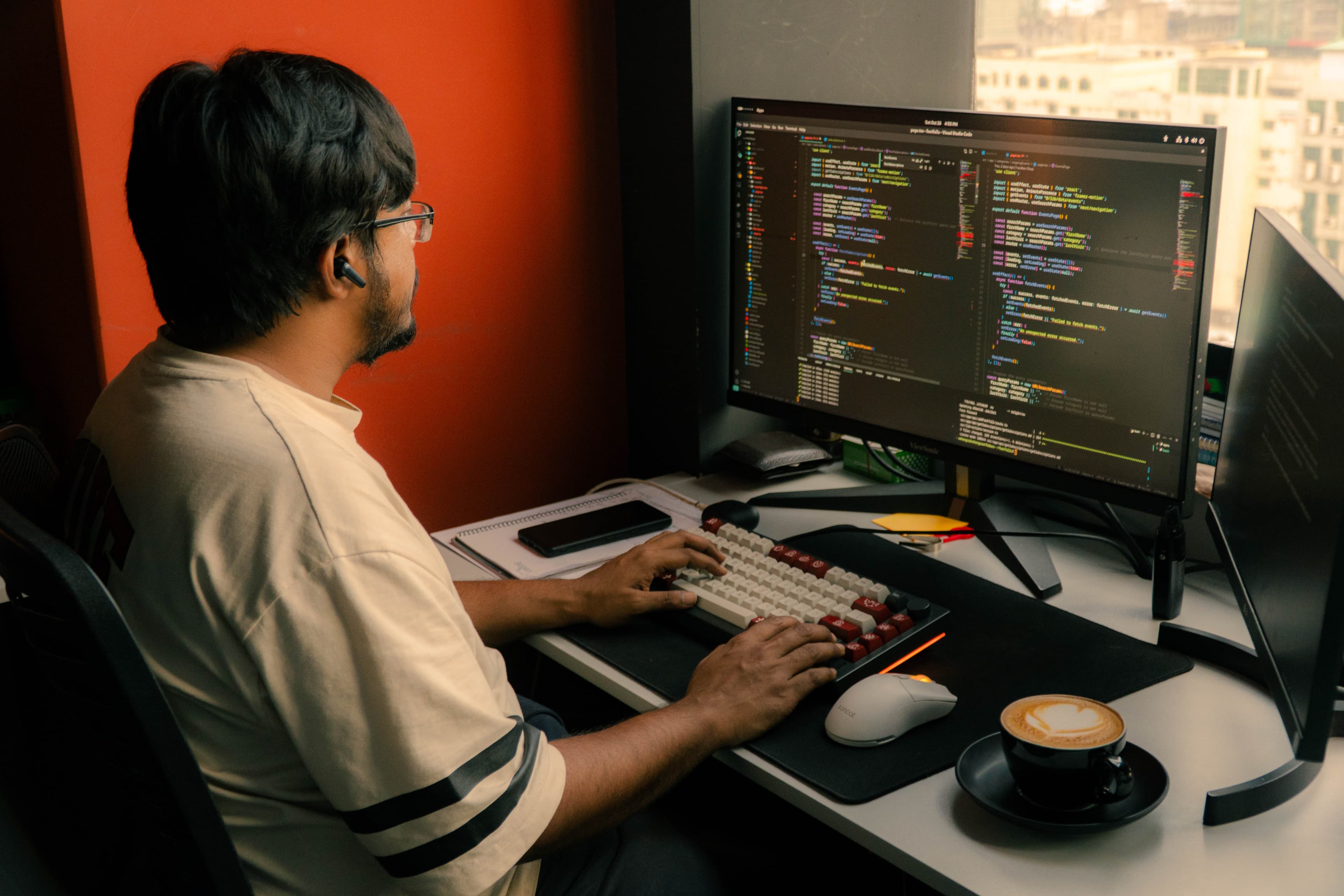 Mashrur Nazrul Mashfi coding at a desktop workspace beside a city view.