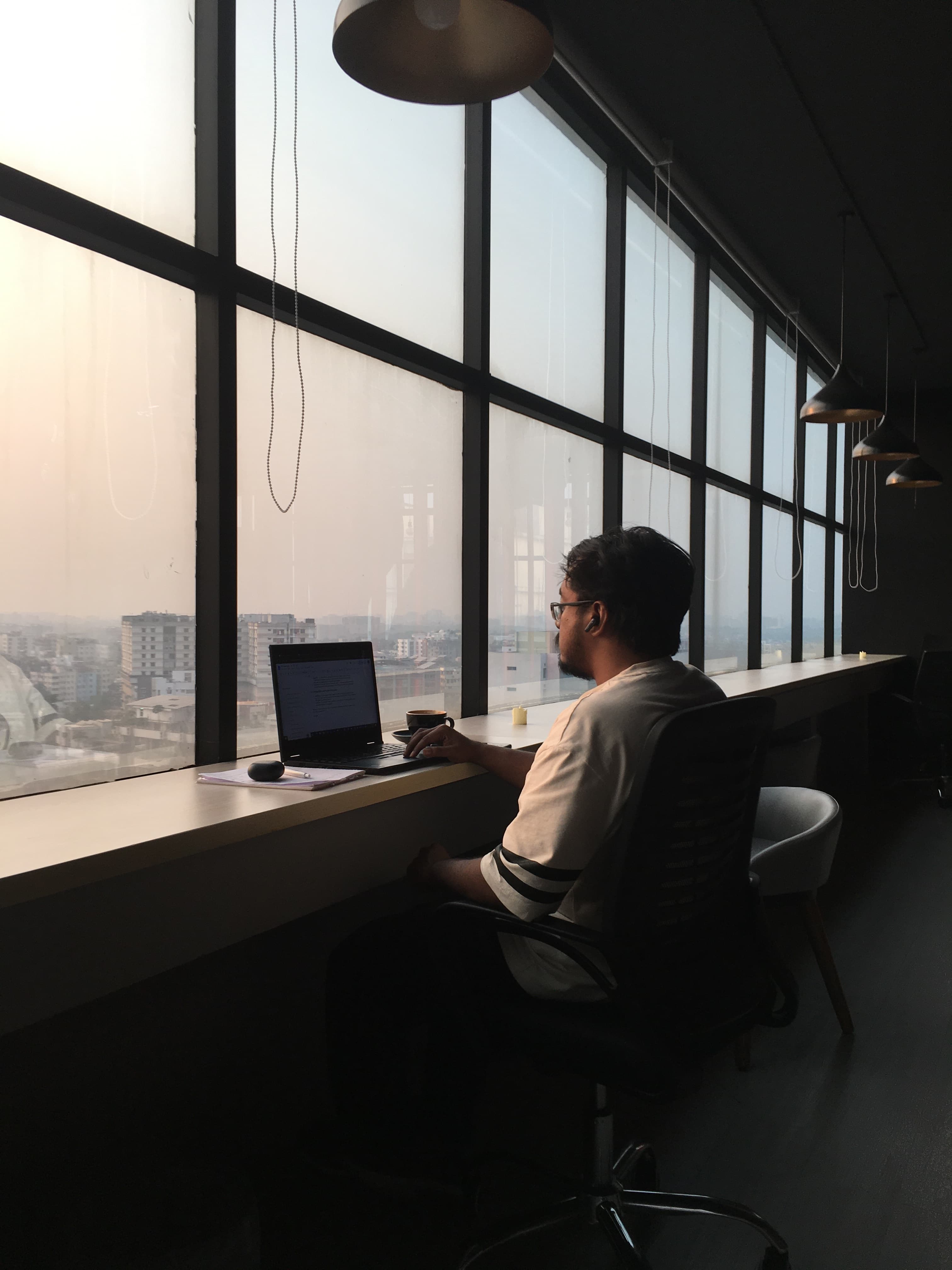 Mashrur Nazrul Mashfi working by a large window overlooking the city.